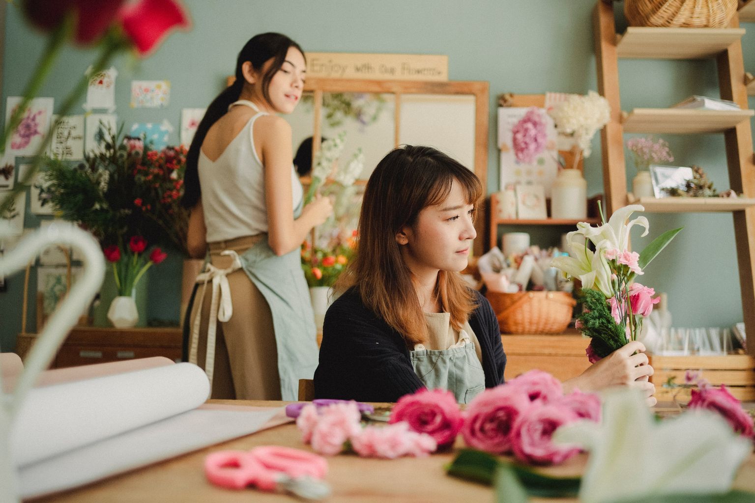 Focused Asian florist arranging bouquet of flowers for event while working with assistant in floral store